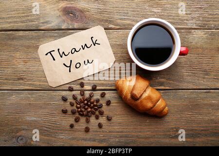 Tasse Kaffee, frisches Croissant und Karte mit Text Danke auf Holztisch, Draufsicht Stockfoto