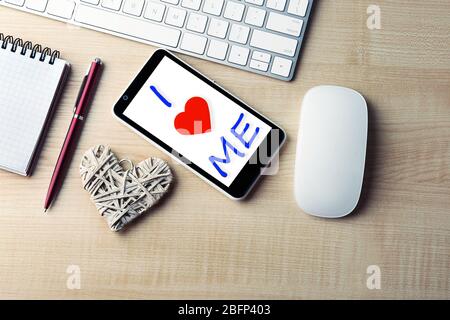 Love Yourself Konzept. Computer-Peripheriegeräte mit weißem Weidenherz, Notebook und Handy auf hellem Holztisch Stockfoto