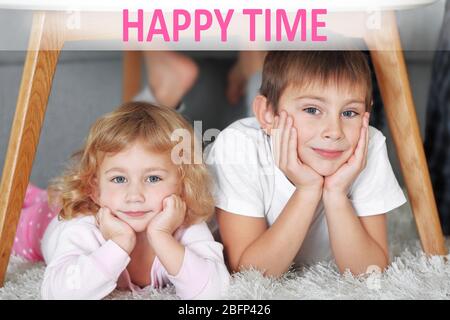 Text Happy Time und süße kleine Kinder spielen unter dem Tisch Stockfoto