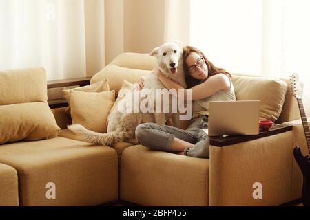 Schöne Frau sitzt auf dem Sofa und umarmt einen Hund. Stockfoto