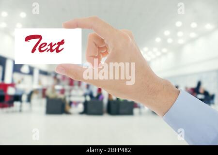 Männliche Hand mit weißer, unbeschriftete Karte auf verschwommenem Café Stockfoto