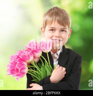 Niedlicher Junge mit Blumen auf verschwommenem Hintergrund. Bildungskonzept. Stockfoto