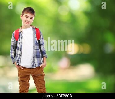 Niedlicher Junge mit Rucksack auf verschwommenem grünen Hintergrund. Schulkonzept. Stockfoto