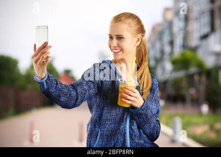 Schöne sportliche Frau, die Selfie auf verschwommenem Stadtstraßenhintergrund nimmt. Sportkonzept. Stockfoto