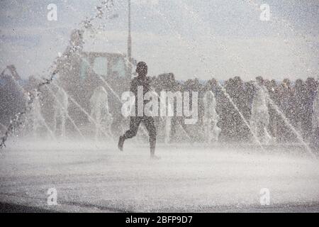 Silhouette der Kinder springen in kühlen Brunnen Wasser. Ein Junge spielt in Wasserfontänen. Glückliche Kinder spielen glücklich in der Stadt Brunnen an einem heißen Tag Stockfoto