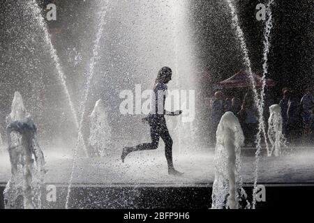 Silhouette der Kinder springen in kühlen Brunnen Wasser. Ein Junge spielt in Wasserfontänen. Glückliche Kinder spielen glücklich in der Stadt Brunnen an einem heißen Tag Stockfoto