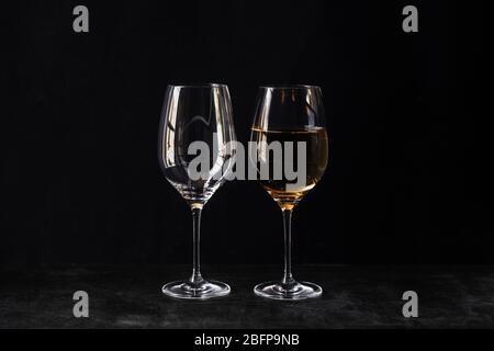 Zwei Gläser für Wein auf schwarzem Hintergrund. Eine leere, die zweite Hälfte voll Weißwein. Der Begriff des Otimisten und des Pessimisten. Mit interessant Stockfoto