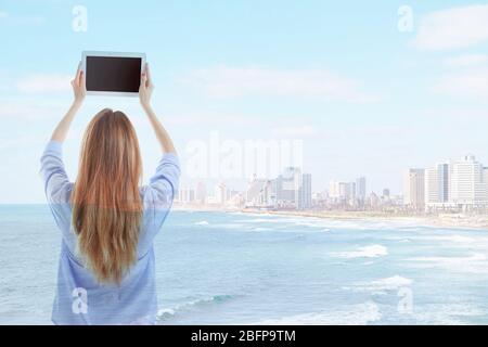 Konzept der virtuellen Technologien. Schönes Meer mit Stadt und junge Frau mit Tablet Stockfoto