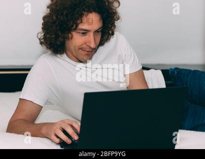 Mann mit lockigen Haaren arbeitet von zu Hause aus während der Quarantäne Zeit von Coronavirus. Bestellen Sie Lebensmittel online. Lustige Stimmung. Konzept „Bleib zu Hause“. Online-Chat. Remote Stockfoto