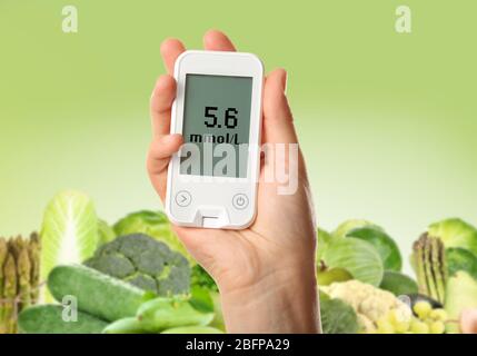 Männliche Hand hält Glucometer mit Gemüse und Obst auf grünem Hintergrund. Diabetes-Konzept Stockfoto