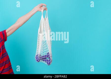 Weiße Netztasche mit Hanteln in der Hand auf blauem Hintergrund mit Kopierfläche. Stockfoto