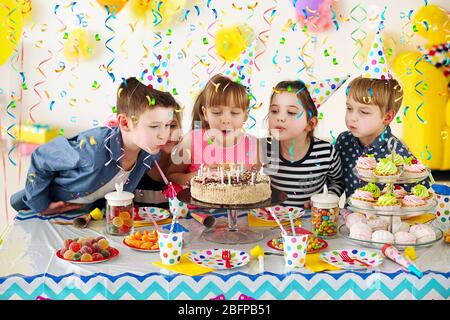 Glückliche Gruppe von Kindern, die Kerzen auf Kuchen bei der Geburtstagsfeier blasen Stockfoto