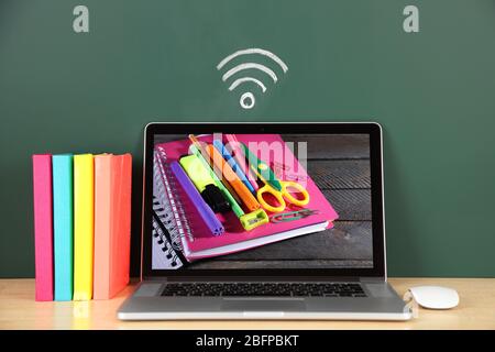 Laptop mit Schreibwaren Tapete auf dem Bildschirm gegen Tafel. WI-FI-Zeichen im Hintergrund. Konzept des Schullehrers. Stockfoto