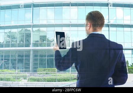 Technologien des Zukunftskonzepts. Junger Mann im Anzug mit Tablet auf modernen Bürogebäude Hintergrund Stockfoto
