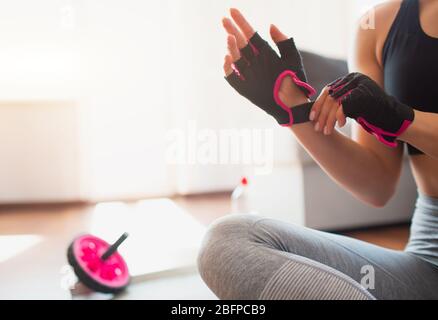 Junge Frau, die während der Quarantäne im Zimmer Sport macht. Sporthandschuhe an die Hände legen. Vorbereitung auf das Heimtraining. Stockfoto