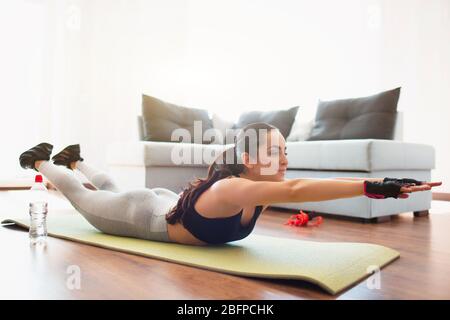 Junge Frau, die während der Quarantäne im Zimmer Sport macht. Auf Matte legen und mit den Händen nach vorne strecken. Heimübungen ohne Ausrüstung. Stockfoto