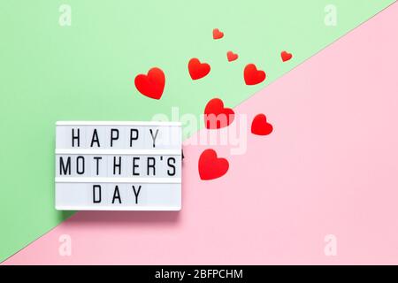 Festliches Konzept. Leuchttafel mit Inschrift Happy Mother's Day, viele rote Herzen in verschiedenen Größen auf pastellfarbenem Hintergrund rosa und grün, Kopierraum. H Stockfoto