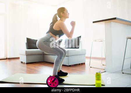 Junge Frau, die während der Quarantäne im Zimmer Sport macht. Hocken Sie auf der Yogamatte im Zimmer. Konzentriertes Training. Stockfoto