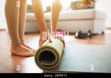 Junge Frau, die während der Quarantäne im Zimmer Yoga-Training macht. Schnitt niedrige Ansicht von barfüßigen Mädchen Rollen Yoga-Matte nach Abschluss Stretching oder Training. Stockfoto