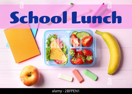 Konzept des Schulmahls. Lunchbox, Essen und Schreibwaren auf Holzhintergrund Stockfoto