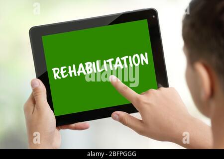 Recovery-Konzept. Mann mit Tablet, Nahaufnahme. Word REHABILITATION auf dem Bildschirm Stockfoto