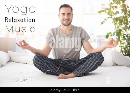 Junger Mann, der beim morgendlichen Yoga-Training auf dem Bett Musik hört. Konzept der Melodie für die Meditation Stockfoto