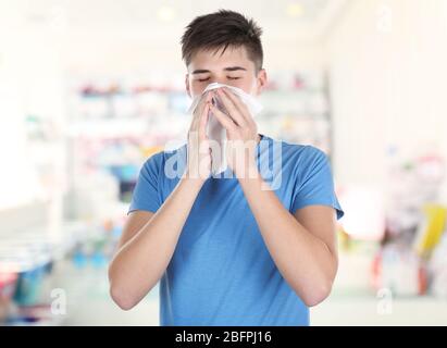 Allergien oder Kälte Konzept. Junger Mann, der in der Apotheke mit der Nase auf das Gewebe bläst Stockfoto