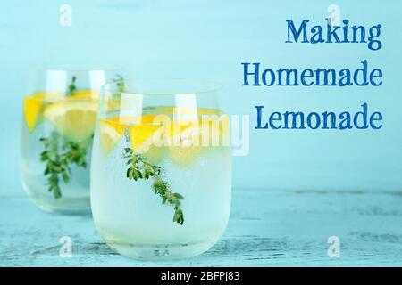 Ein Glas erfrischendes Getränk mit Zitrone und Thymian auf einem Holztisch. Text HERSTELLUNG HAUSGEMACHTE LIMONADE auf Hintergrund Stockfoto