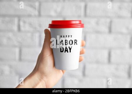 Frau, die Pappbecher mit Text GLÜCKLICH TAG ARBEIT auf Backstein Wand Hintergrund, Nahaufnahme Stockfoto