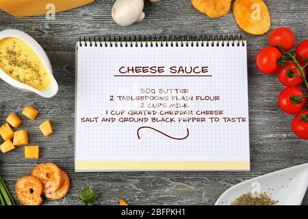 Notizbuch mit Käsesauce Rezept und Lebensmittel auf Holzhintergrund Stockfoto