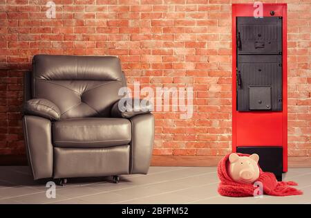 Energieeinsparkonzept. Festbrennstoff-Kessel und Sparschwein mit Sessel auf Backstein Wand Hintergrund Stockfoto