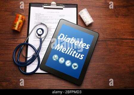 Konzept der Gesundheitsfürsorge. Tablette mit Text DIABETES MELLITUS, Krankengeschichte und Stethoskop auf Holzhintergrund Stockfoto
