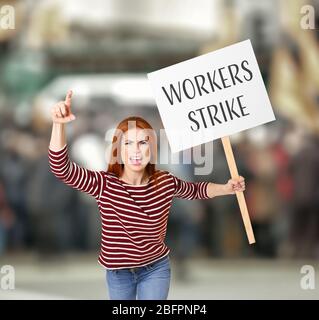 Junge Frau mit Schild und verschwommener Menge auf Hintergrund. Konzept des Streiks der Arbeiter Stockfoto