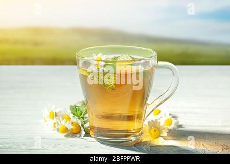 Heißer Kamillentee in Tasse mit Blumen auf Holztisch im Freien Stockfoto