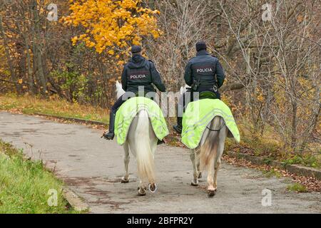 Polizei im Herbst-Stadtpark, Rückansicht. Polizeiaufschrift auf der Rückseite. Zwei spanische Polizisten zu Pferd patrouillieren im Park. Stockfoto