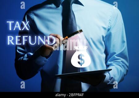 Mann mit Lupe und Tablet auf dunklem Hintergrund. Konzept der Steuerrückerstattung Stockfoto