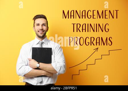 Junger Mann hält Zwischenablage und TEXTMANAGEMENT TRAININGSPROGRAMME mit Diagramm auf gelbem Hintergrund Stockfoto