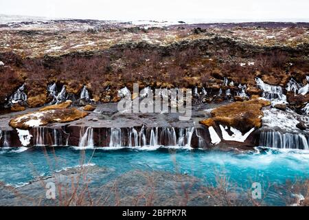 Hraunfossar Wasserfälle, die im Winter in den von Gletschern gespeisten Hvita Fluss in Island stürzen Stockfoto