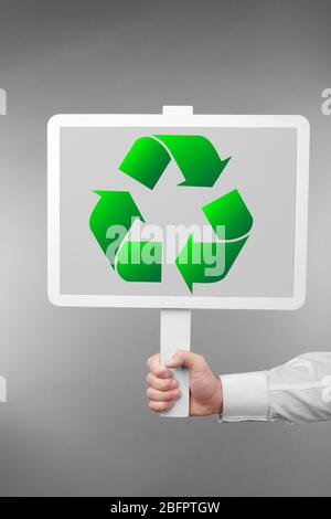 Mann mit Schild mit Zeichen des Recyclings auf grauem Hintergrund. Ökologie und Umweltschutz Stockfoto