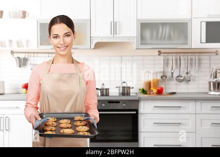 Junge Frau in Schürze hält Tablett mit Plätzchen in der Küche zu Hause Stockfoto