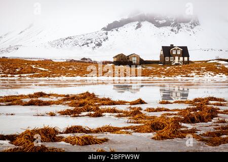 Amtmannshusid Haus in Arnarstapi auf der Snaefellsnes Halbinsel in Island an einem eisigen und verschneiten Wintertag in Orange- und Weißtönen Stockfoto