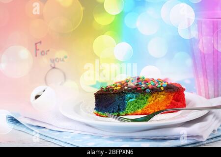 Teller mit Stück Regenbogenkuchen auf dem Tisch Stockfoto