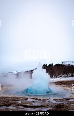 Geysir, Island - Strokkur heiße Quelle im Geysir Geothermie-Gebiet bricht an einem bewölkten Tag im Winter aus Stockfoto