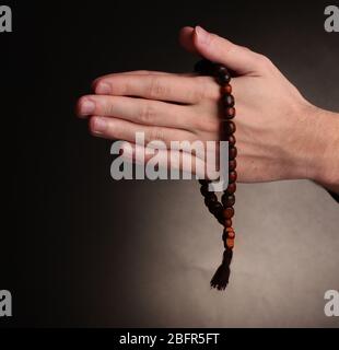 Hände halten hölzernen Rosenkranz auf grauem Hintergrund Stockfoto