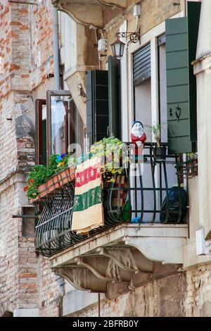 Ein Gartenzwerg steht Wache über den Blumen auf diesem Balkon über einer Gasse in Venedig, Italien. gnomo Stockfoto