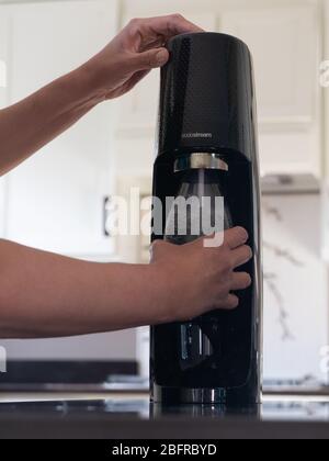 Latina Frau hält eine wiederverwendbare Sodastream Flasche, wie sie kohlensäurehaltige das Wasser enthält. Fotografiert in einer modernen Küche mit geringer Schärfentiefe. Stockfoto