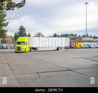 Gelb Big Rig klassische Motorhaube Industrie Diesel-Sattelschlepper mit Kühlschrank Sattelanhänger läuft auf dem LKW-Stopp-Parkplatz vorbei an anderen geparkten Truc Stockfoto