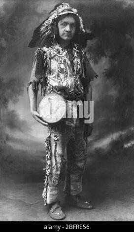 Indianer/Indianer, c.. 1921. Er wurde als 'Chief Running Deer' identifiziert. Er hat eine Revolverpistole im Gürtel und eine Fransentasche hinter seiner schön bemalten Trommel. Dieses Bild wurde in Florida, USA aufgenommen. Dieser Mann könnte in all diese wunderbar Perlen Kleidung und Accessoires für seine Familie und sich selbst gekleidet haben. Aber es ist wahrscheinlicher, dass dies ein Foto für den Verkauf an Touristen war. Sein Name kann gut für die Show auch erfinden worden sein. Amerikanische Touristen liebten romantisierte Bilder der Ureinwohner. Um meine anderen verwandten Bilder zu sehen, Suche: Prestor Vintage West Stockfoto