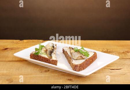 Leckere Sandwiches mit Sprossen auf Teller auf Holztisch auf braunem Hintergrund Stockfoto