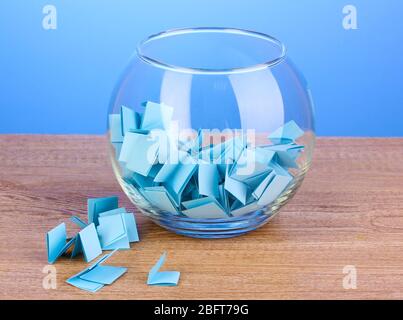 Stücke Papier für Lotterie in Vase auf Holztisch auf blauem Hintergrund Stockfoto